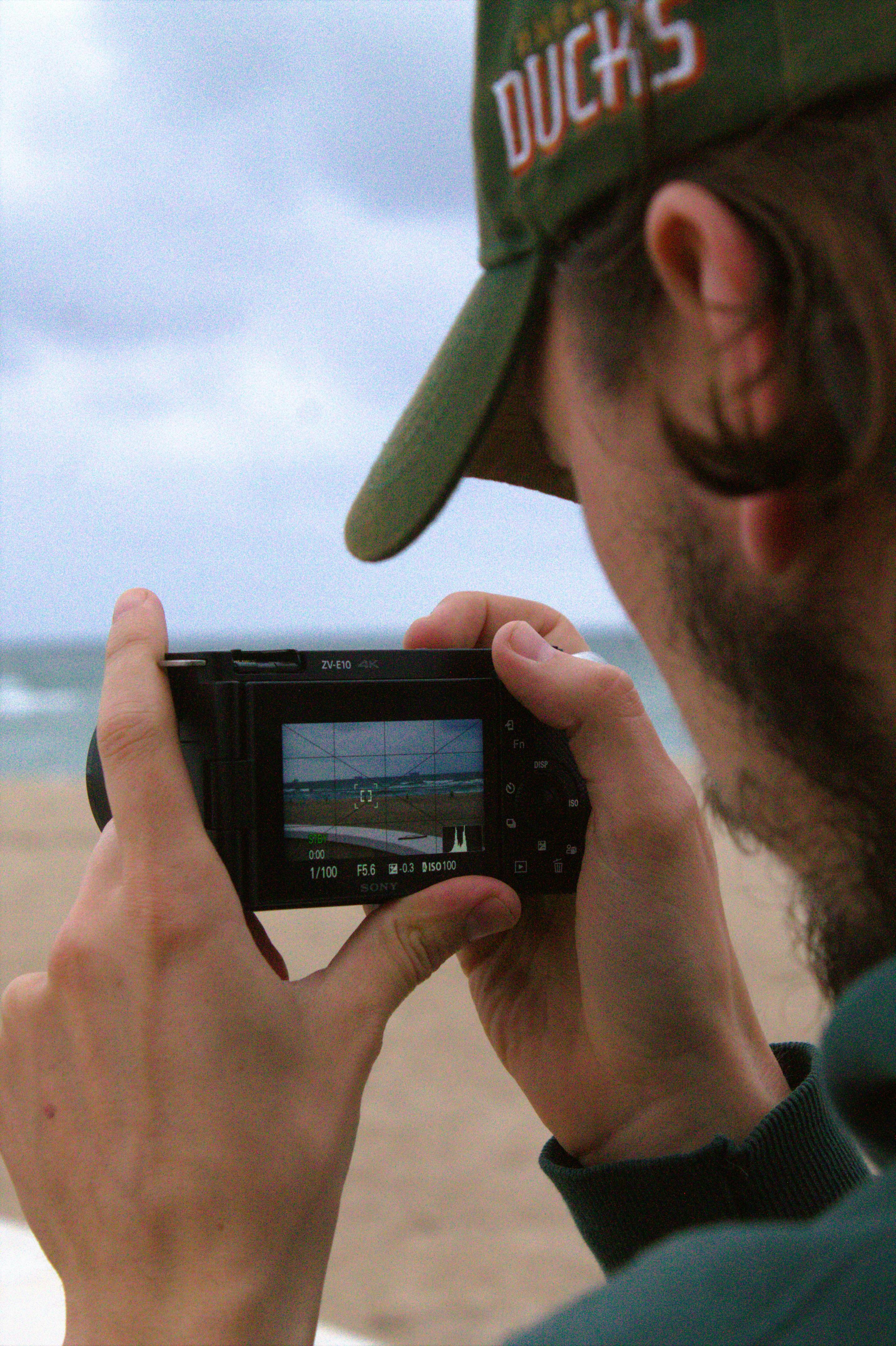 A person taking a photo of a beach scene with a handheld camera.