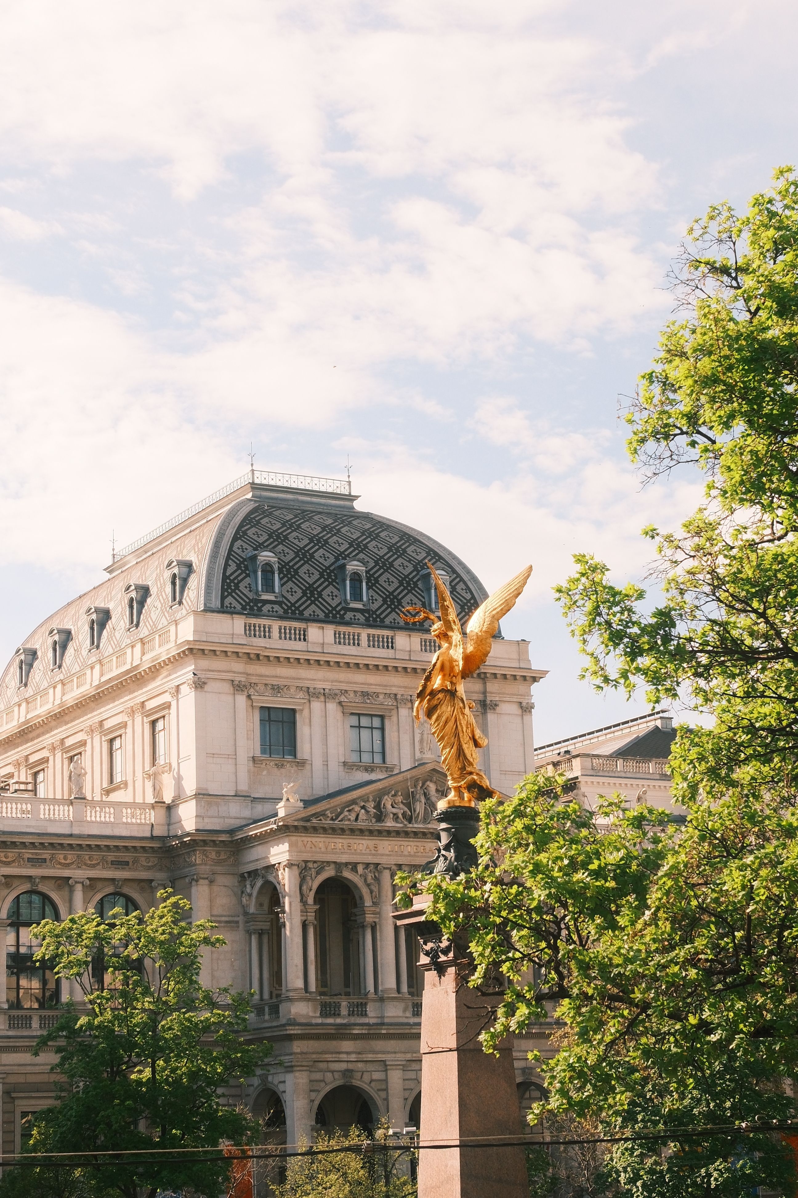 Ornate Baroque building and golden statue set against a clear spring sky in Vienna, Austria.