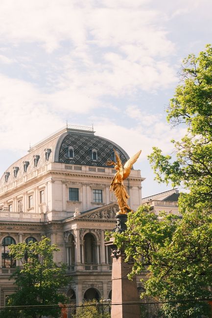 Ornate Baroque building and golden statue set against a clear spring sky in Vienna, Austria.