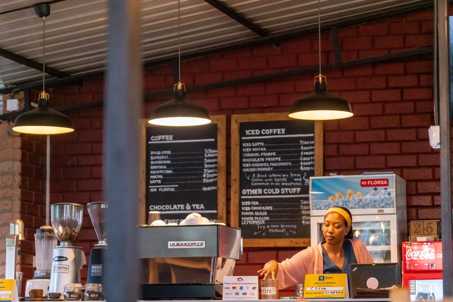 Barista at a cozy coffee shop counter, with espresso machine and menu boards in view.