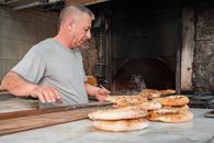 Baker working with fresh bread in a traditional wood-fired oven setting.