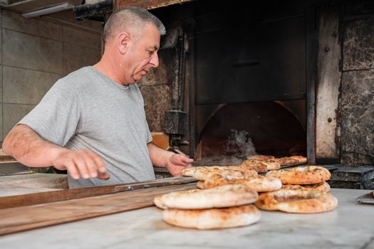 Baker working with fresh bread in a traditional wood-fired oven setting.