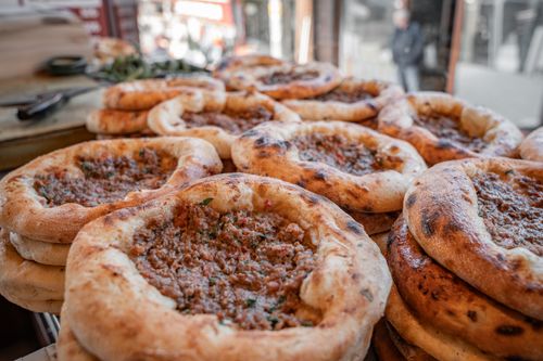 Free Close-up of freshly baked Turkish pide breads filled with minced meat, displayed outdoors at a market. Stock Photo