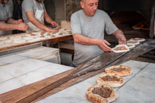 Bakers shaping delicious Turkish pide bread with meat filling in a rustic bakery setting.