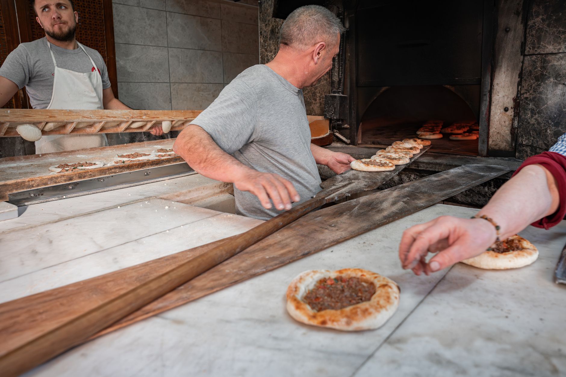 Bakers using wooden paddles to bake traditional Middle Eastern meat pies in a stone oven.