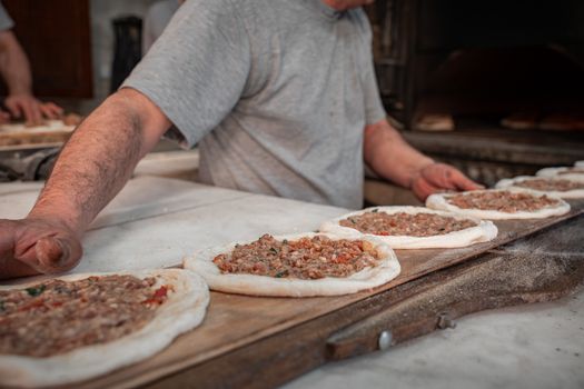 A baker arranging meat-topped flatbreads on a wooden board in a bakery setting.