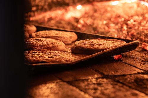 Free Close-up of artisanal bread baking in a rustic stone oven with glowing embers. Stock Photo