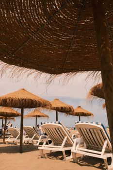 Charming sandy beach with straw umbrellas and sunbeds under a clear sky.