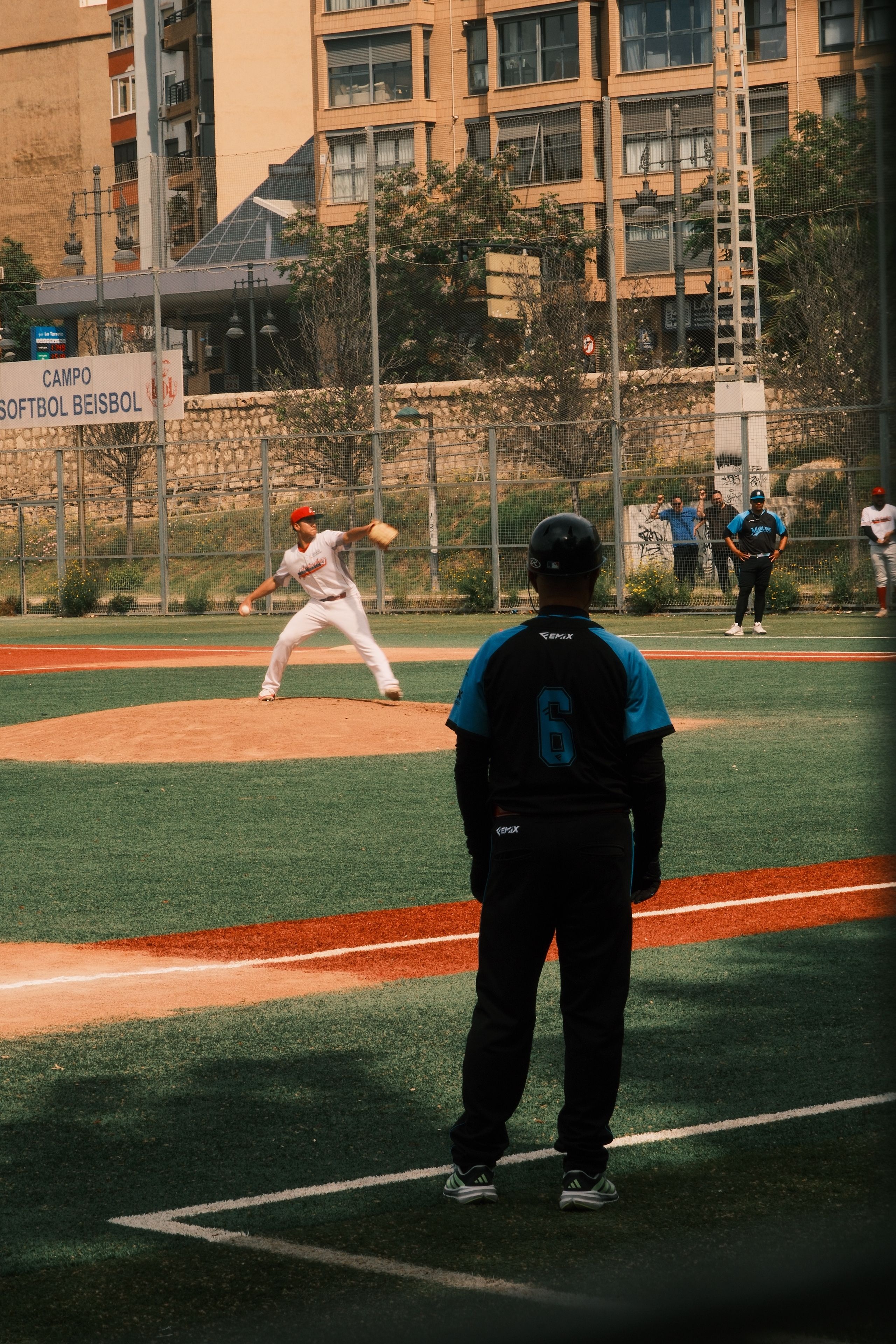 Player prepares to pitch during a baseball game in an urban setting with spectators.