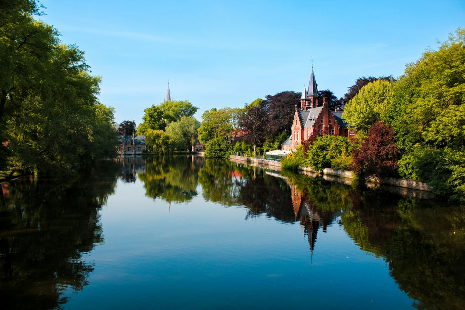 Charming view of a canal with historic architecture and lush greenery in Bruges, Belgium.