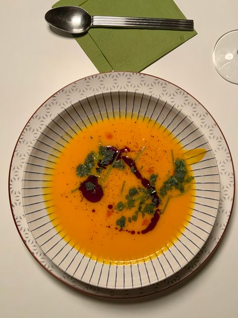 A ceramic bowl of pale golden vegetable soup with shredded cabbage, cauliflower florets, green beans, and rice, steam rising, next to a spoon and a folded cloth napkin.