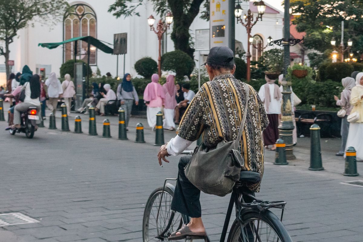 Older cyclist riding through a lively urban public space