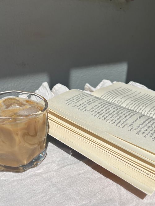 Free A serene setting featuring an open book and iced coffee basking in warm sunlight, perfect for relaxation. Stock Photo