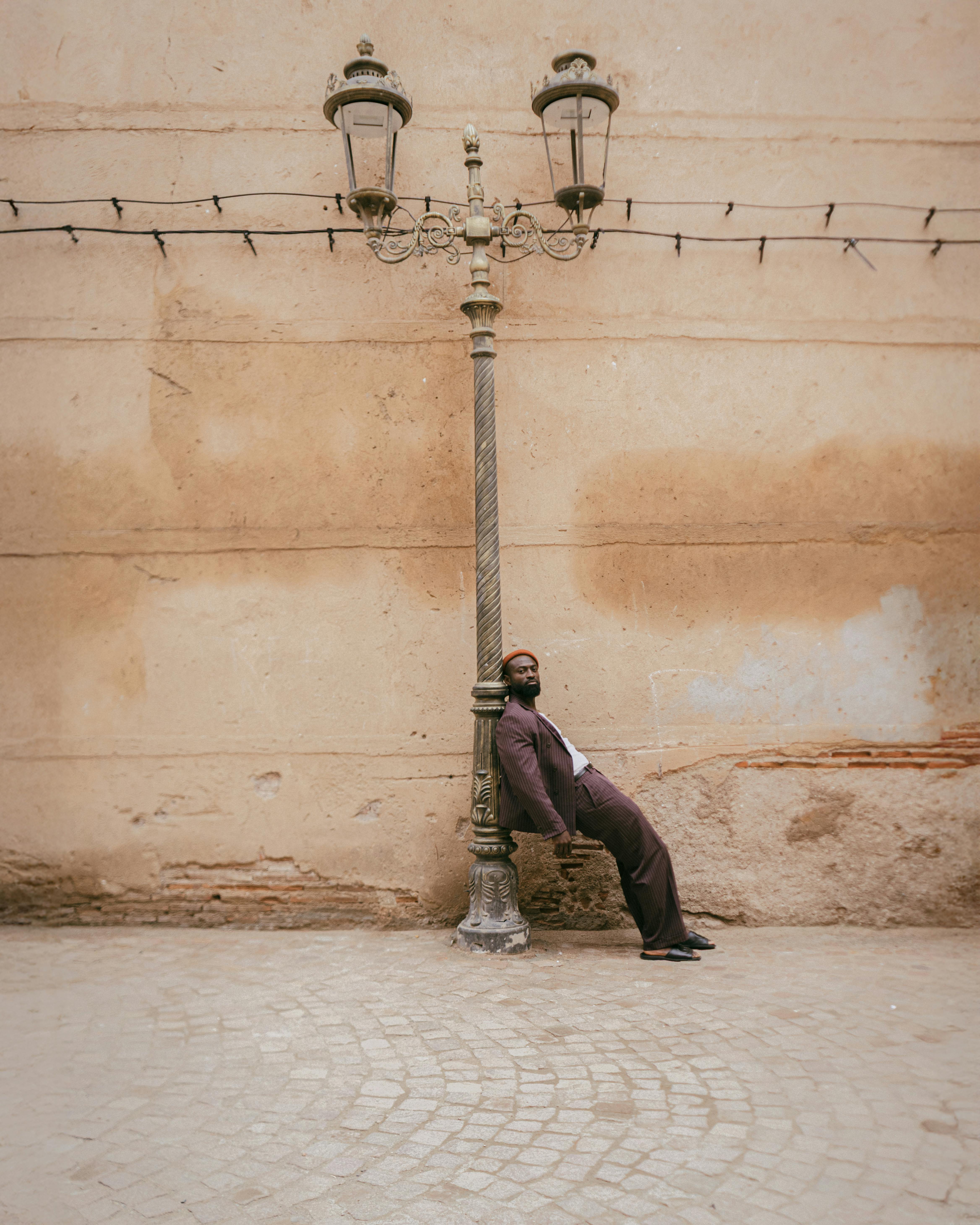 A man leans casually on a vintage lamppost in a Marrakech street, exuding a relaxed urban vibe.