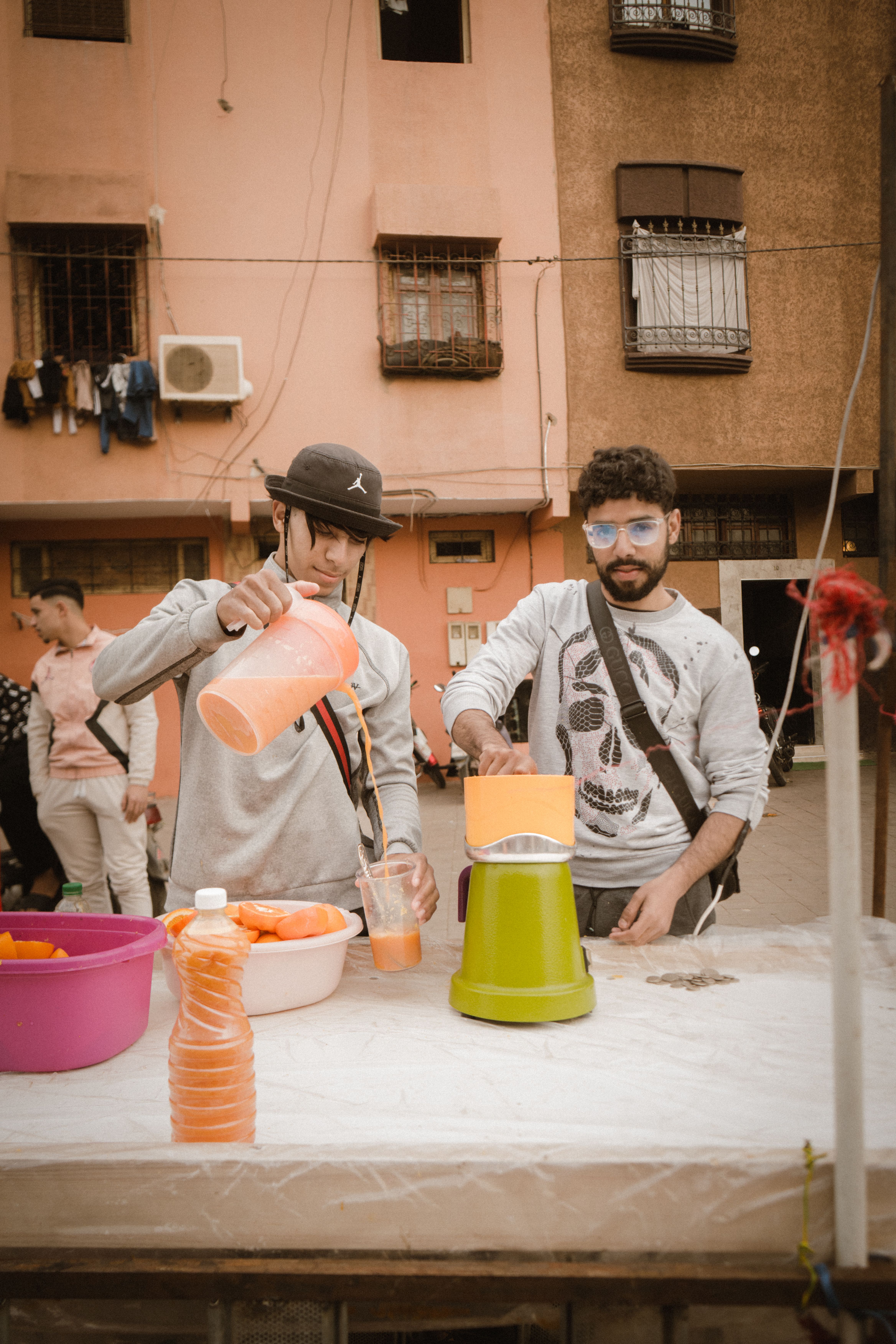 Two vendors at a street market preparing fresh fruit juice with mixers.