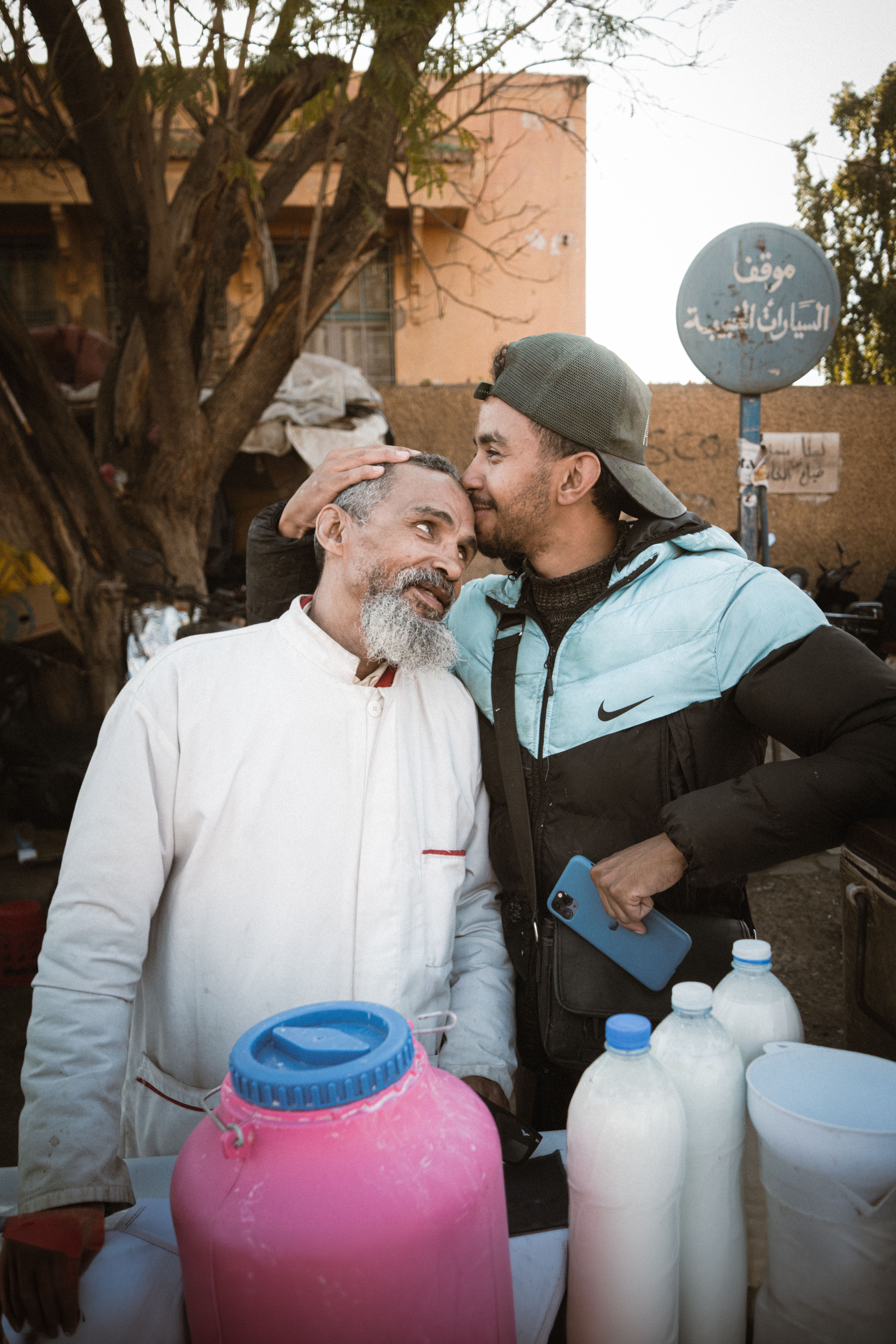 Two men sharing a warm moment at an outdoor market stall with dairy products.