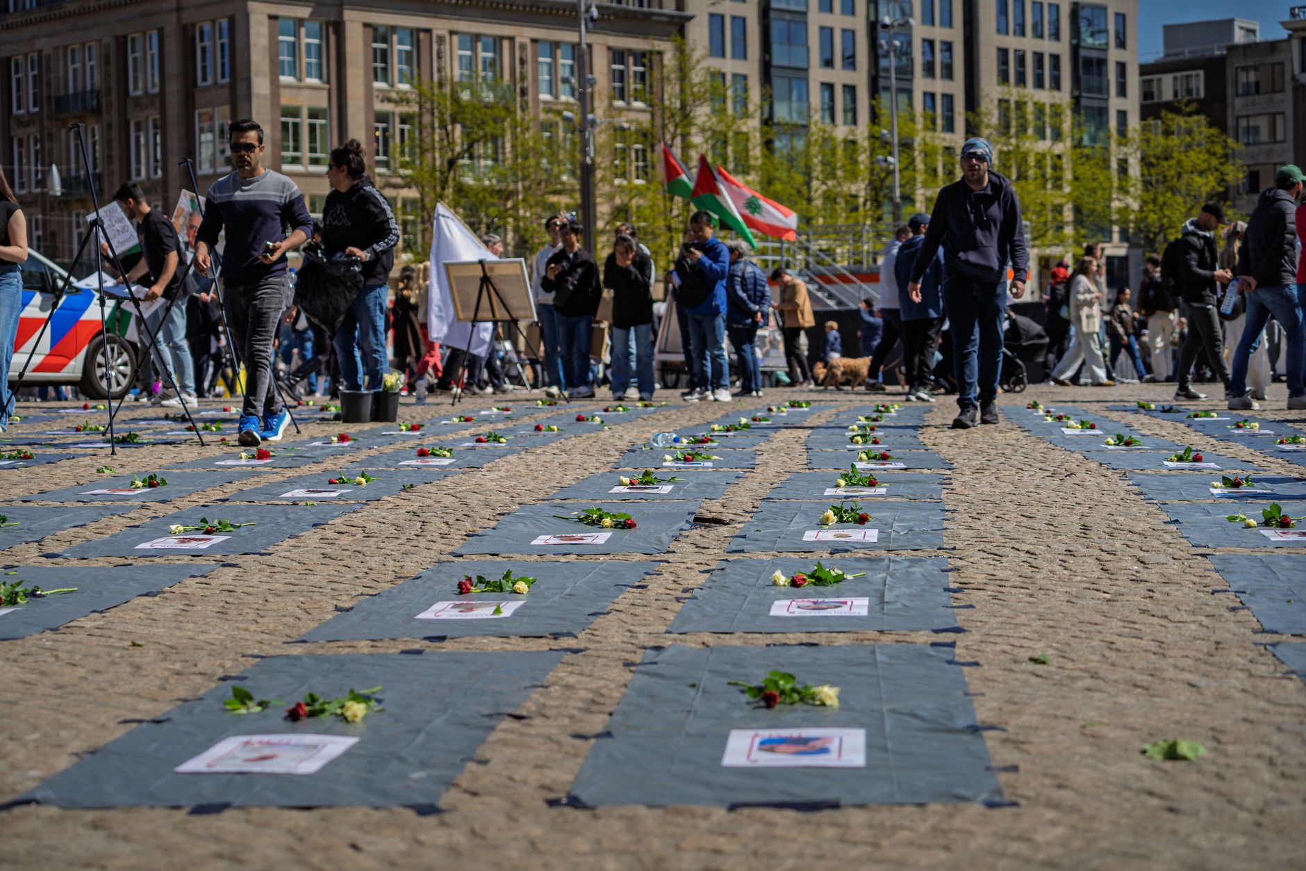 Een openbare herdenkingsbijeenkomst met bloemen en mensen die zich verzamelen op een openbaar plein.