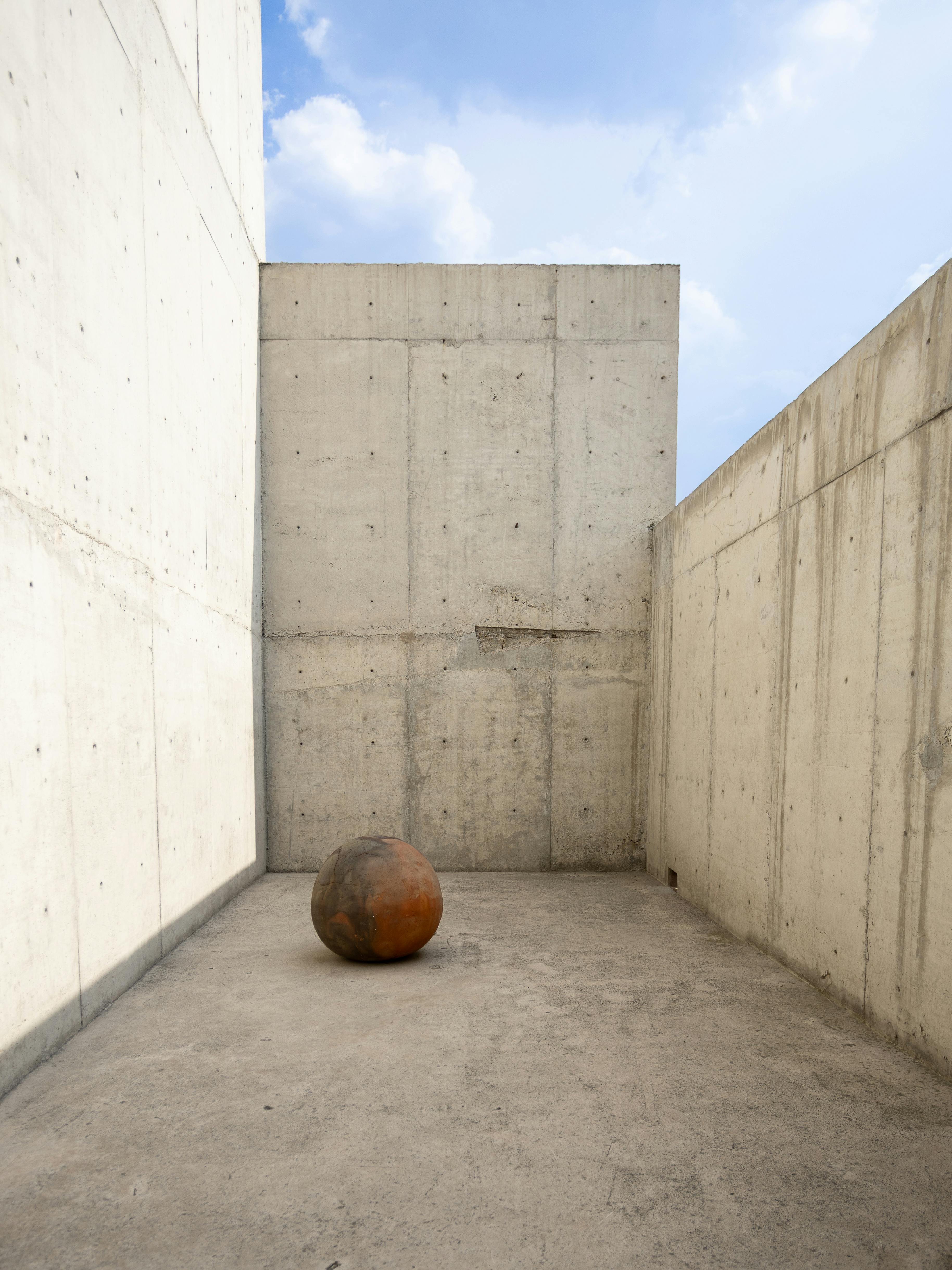Concrete urban setting with a rusted sphere sculpture in Ciudad de México, showcasing minimalist architecture.