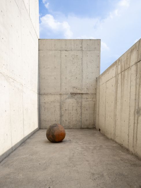 Concrete urban setting with a rusted sphere sculpture in Ciudad de México, showcasing minimalist architecture.