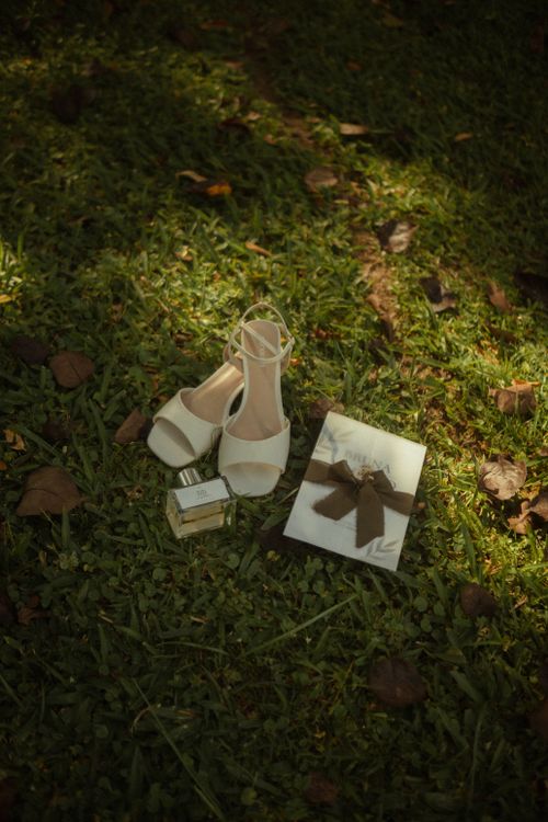 Free Wedding shoes, perfume, and a gift on grass, perfect for bridal preparation shots outdoors. Stock Photo