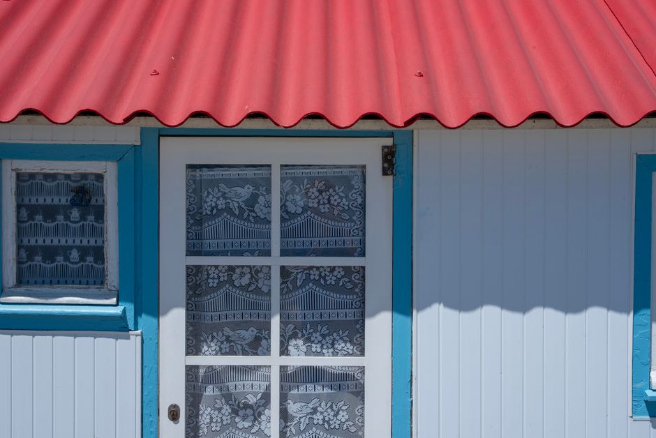 Close-up of a colorful house with a red roof and lace curtains on a sunny day.