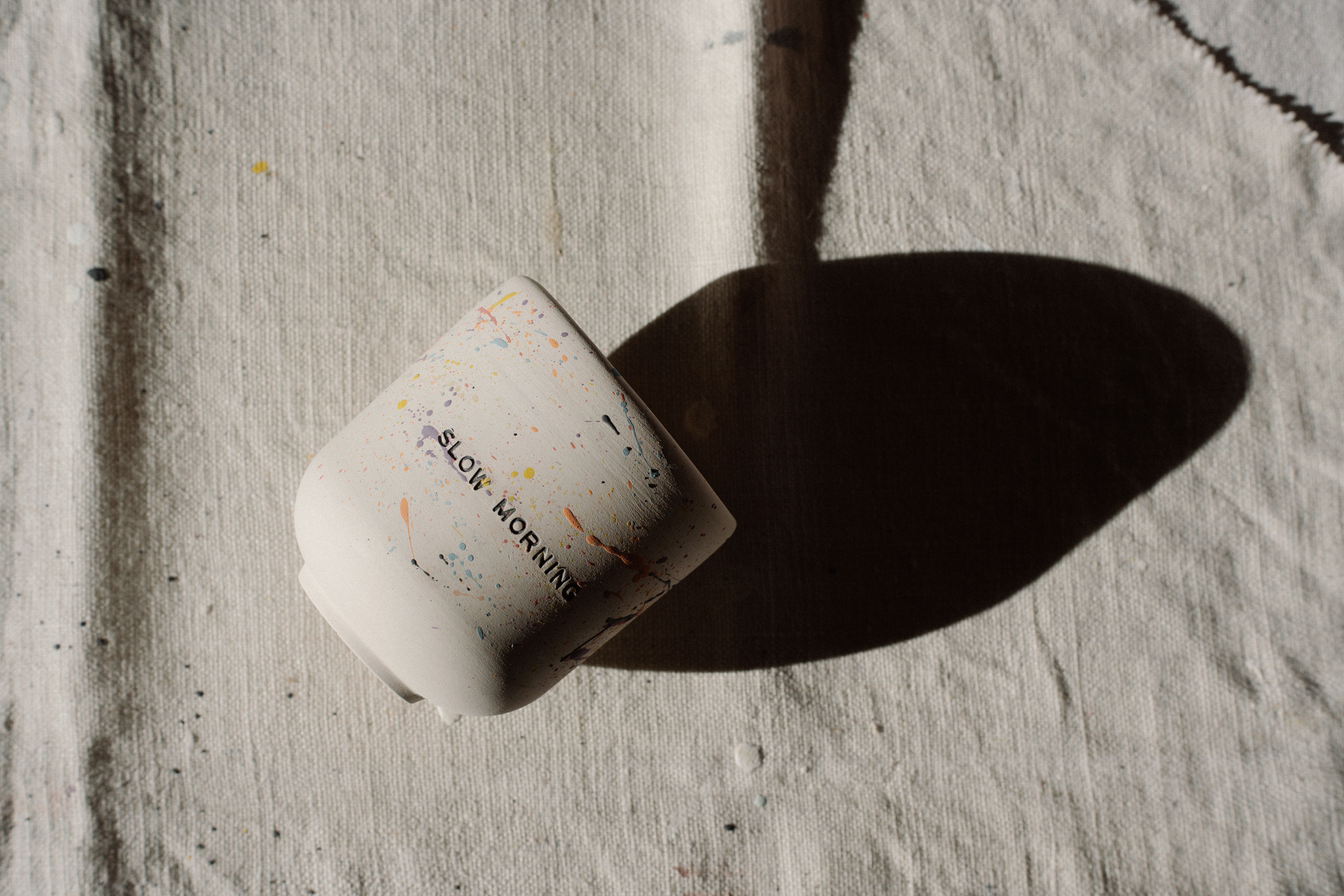 Une tasse en céramique à motifs mouchetés projetant une ombre sur une toile texturée.