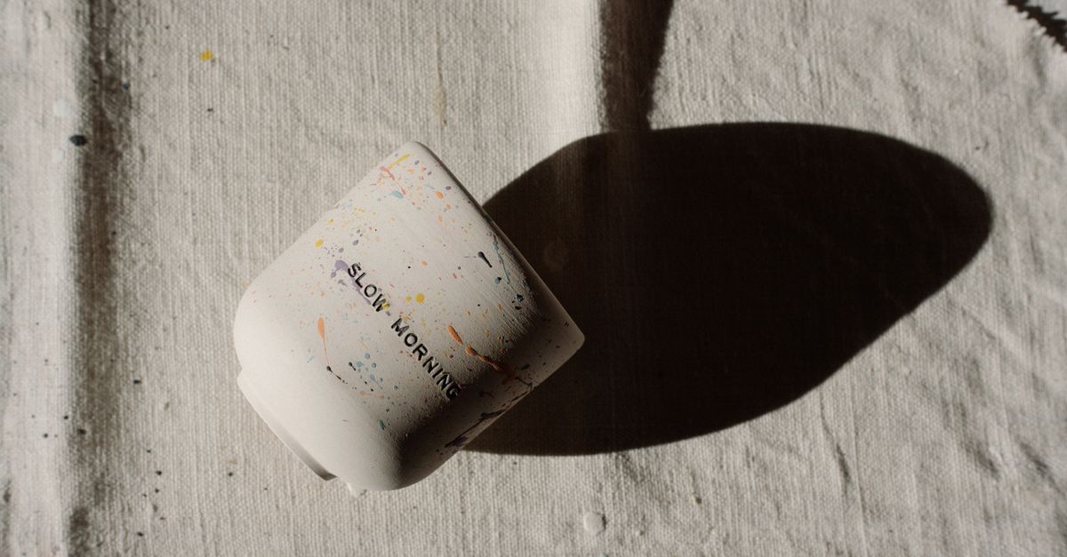 Une tasse en céramique à motifs mouchetés projetant une ombre sur une toile texturée.