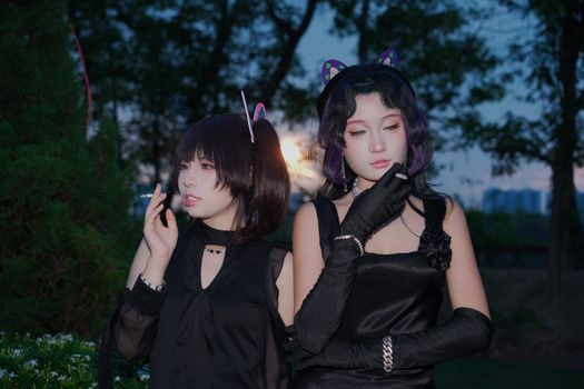 Two women in gothic attire pose with confidence outdoors at dusk in Vietnam.
