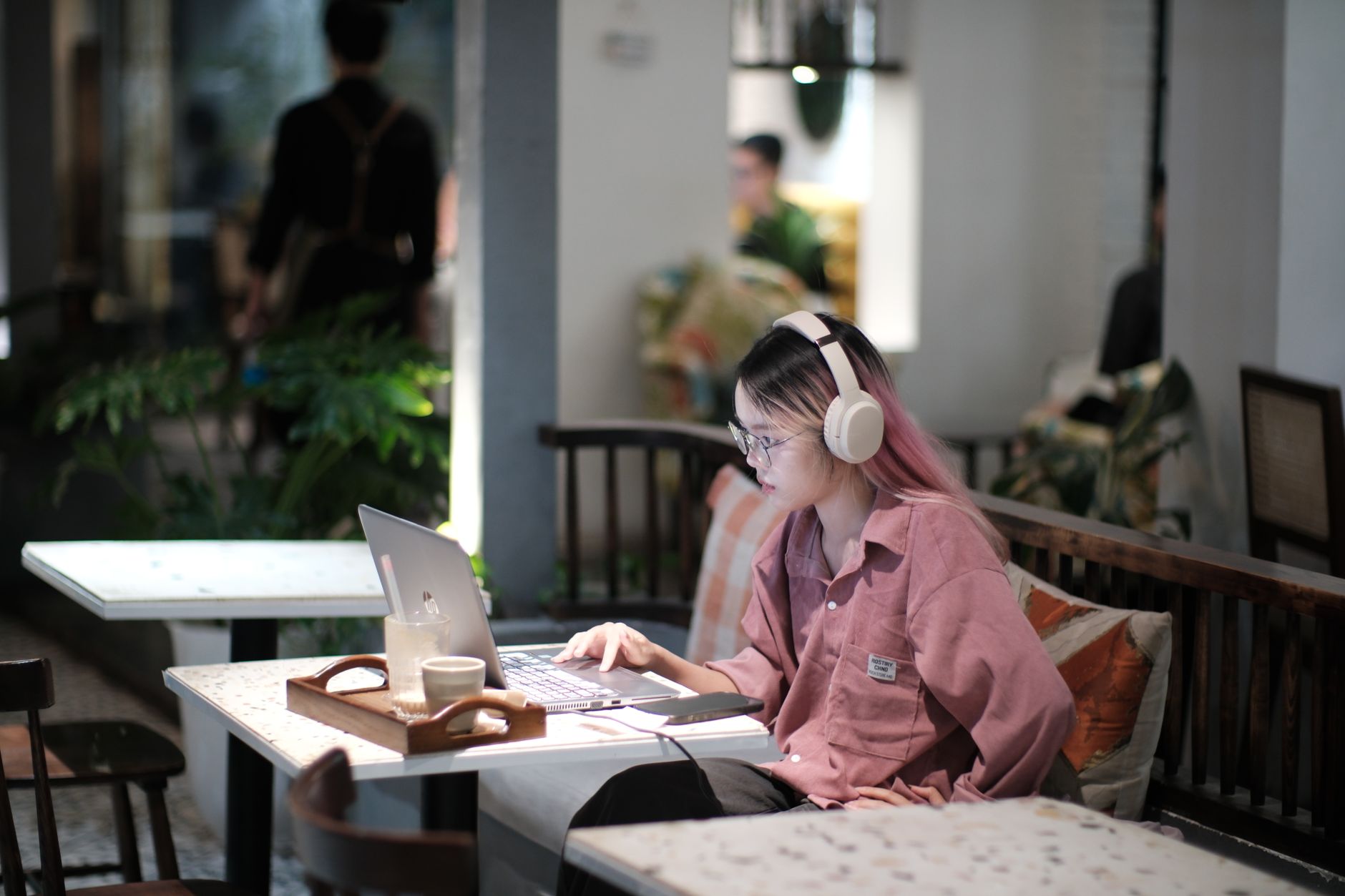 Woman with headphones working on laptop in a cozy Vietnamese cafe setting.
