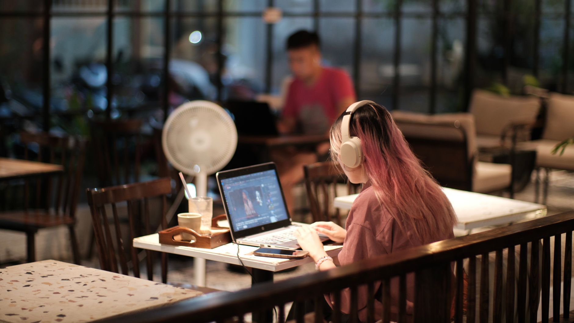 A woman with headphones edits a video on her laptop in a cozy café environment, Vietnam.