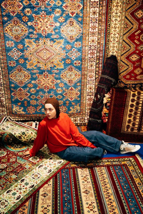 Free Woman sitting among colorful Persian rugs, showcasing intricate patterns and bold colors. Stock Photo