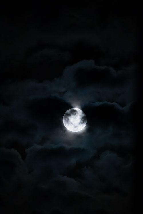 Free A mystical full moon illuminating the night sky through thick, dark clouds, creating a dramatic scene. Stock Photo
