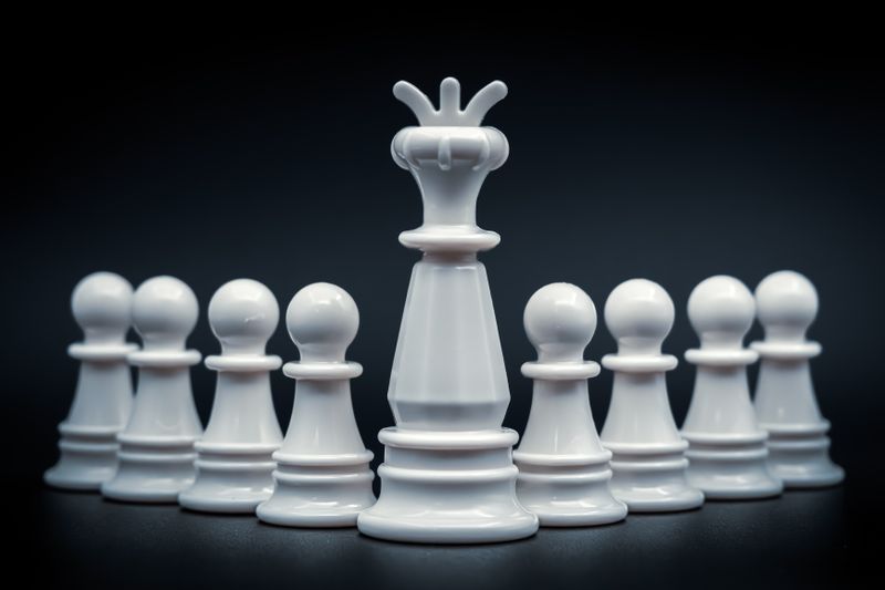 Close-up of white king and pawns on chessboard, symbolizing leadership and strategy.