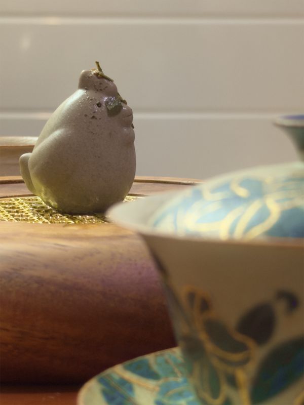 Figurine d'argile « tea pet » sur un plateau à thé en bois derrière un gaiwan