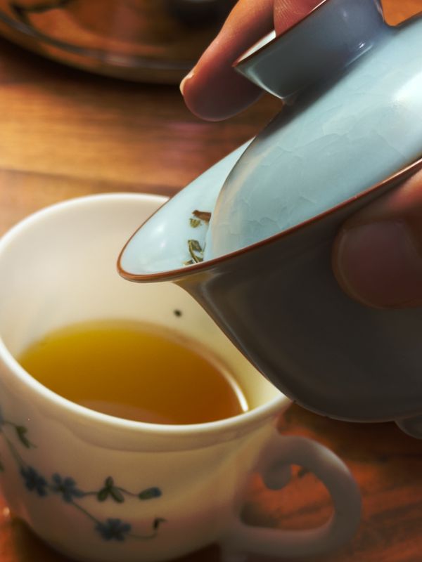 Thé versé d'un gaiwan céladon dans une tasse en porcelaine blanche