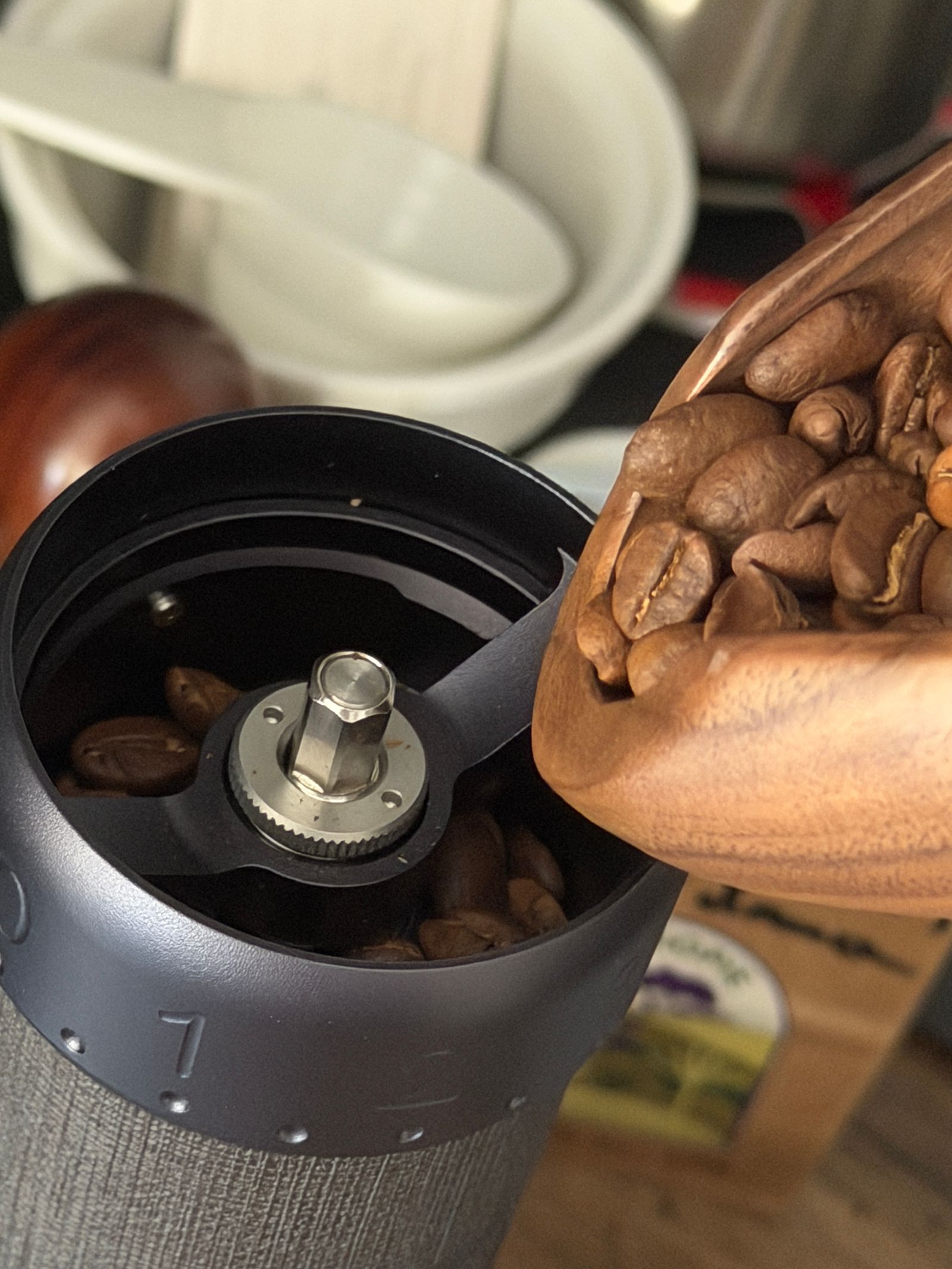 Grains de café versés d'une cuillère en bois dans un moulin manuel