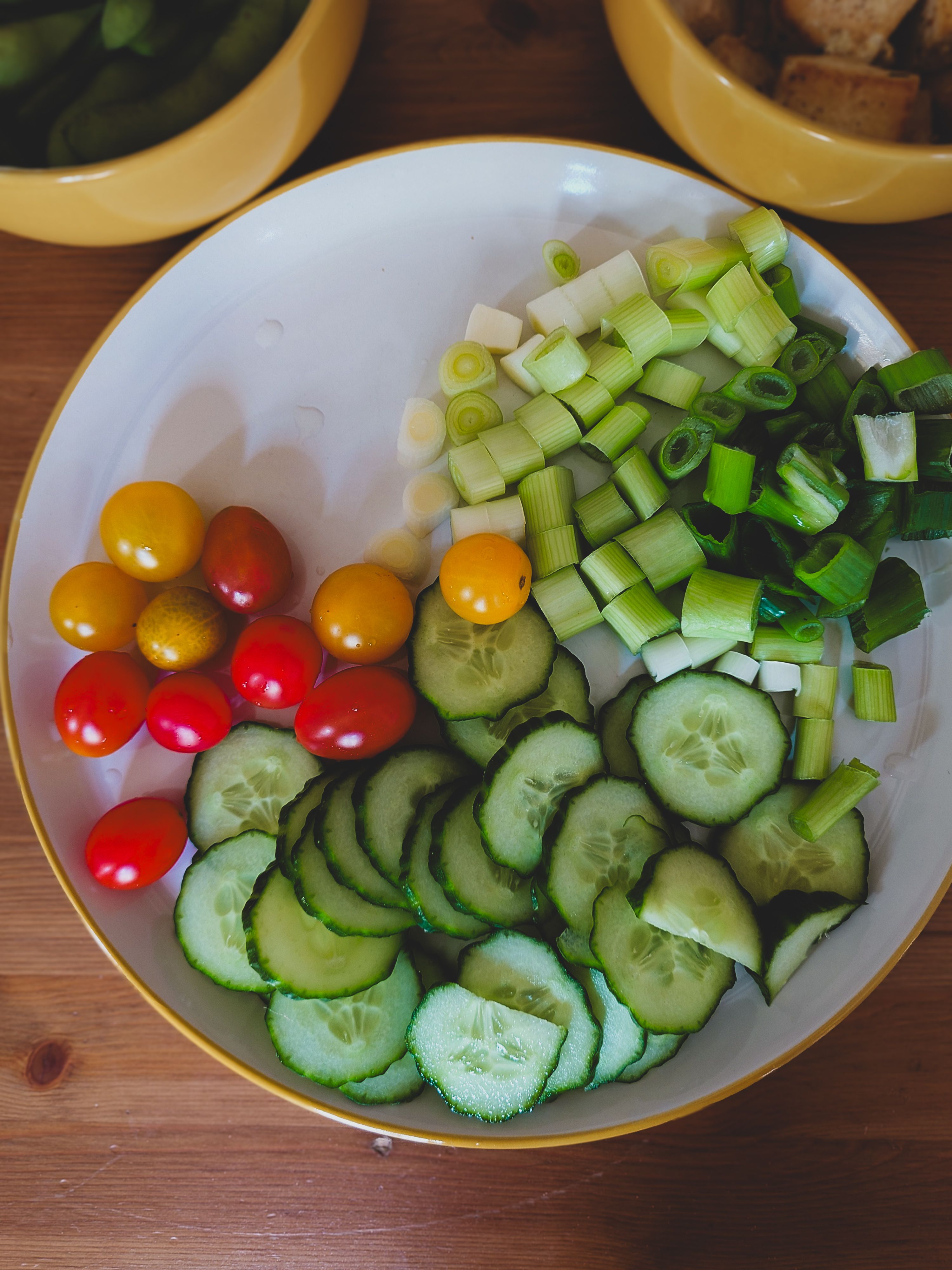 Fresh vegetable salad with cucumbers, cherry tomatoes, and green onions on a wooden table.