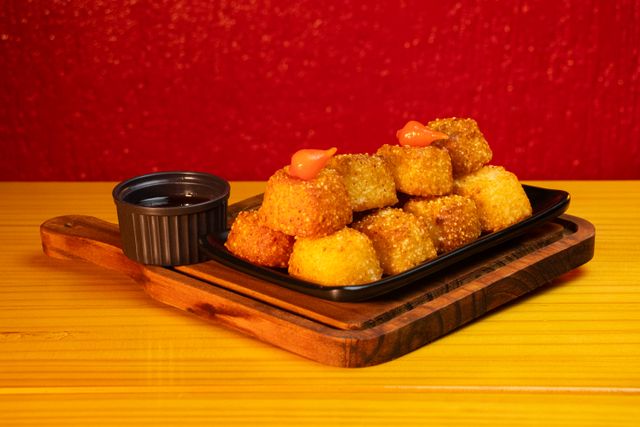 Crispy Brazilian corn snacks served with dipping sauce on a wooden board, ideal for appetizers.