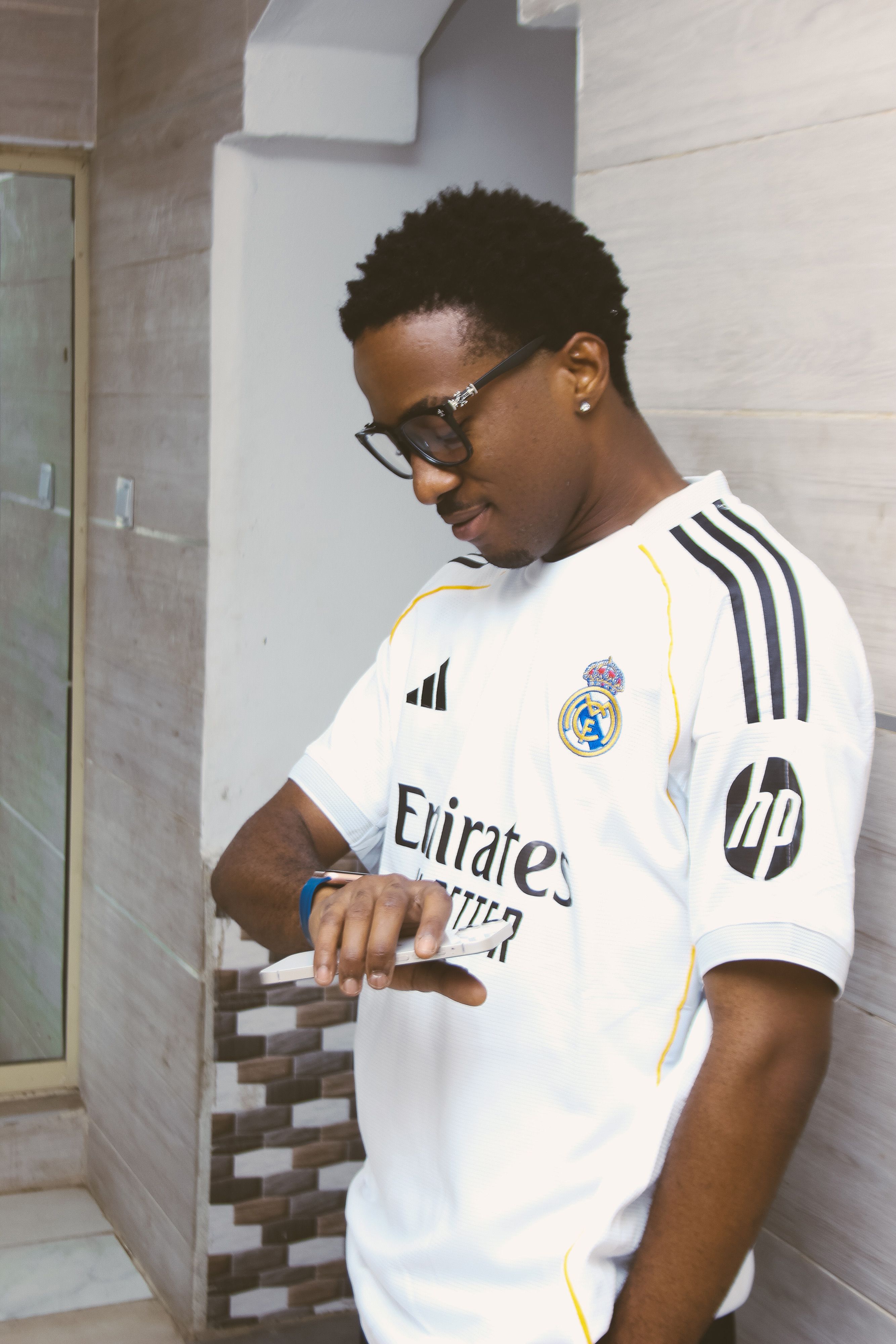 Young man with glasses wearing a football jersey, checking his watch indoors.