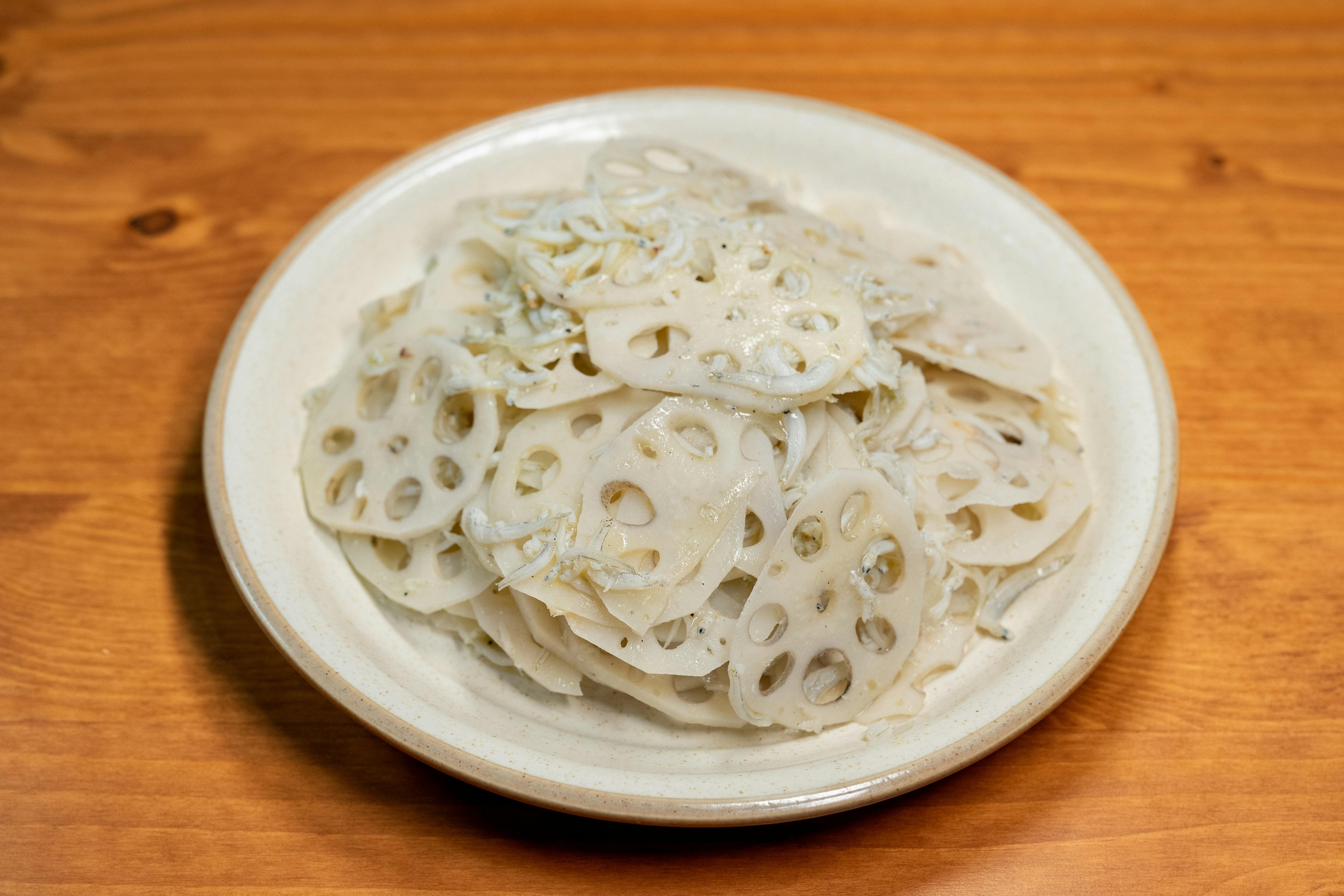 Delicious lotus root salad with small shrimps served on a wooden table, showcasing Asian cuisine.