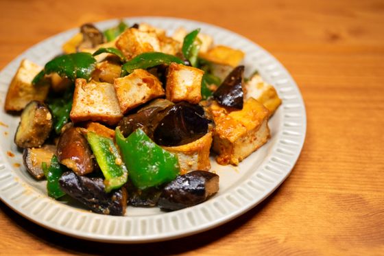Seared tofu cubes with glossy eggplant chunks and green pepper on a ribbed white plate