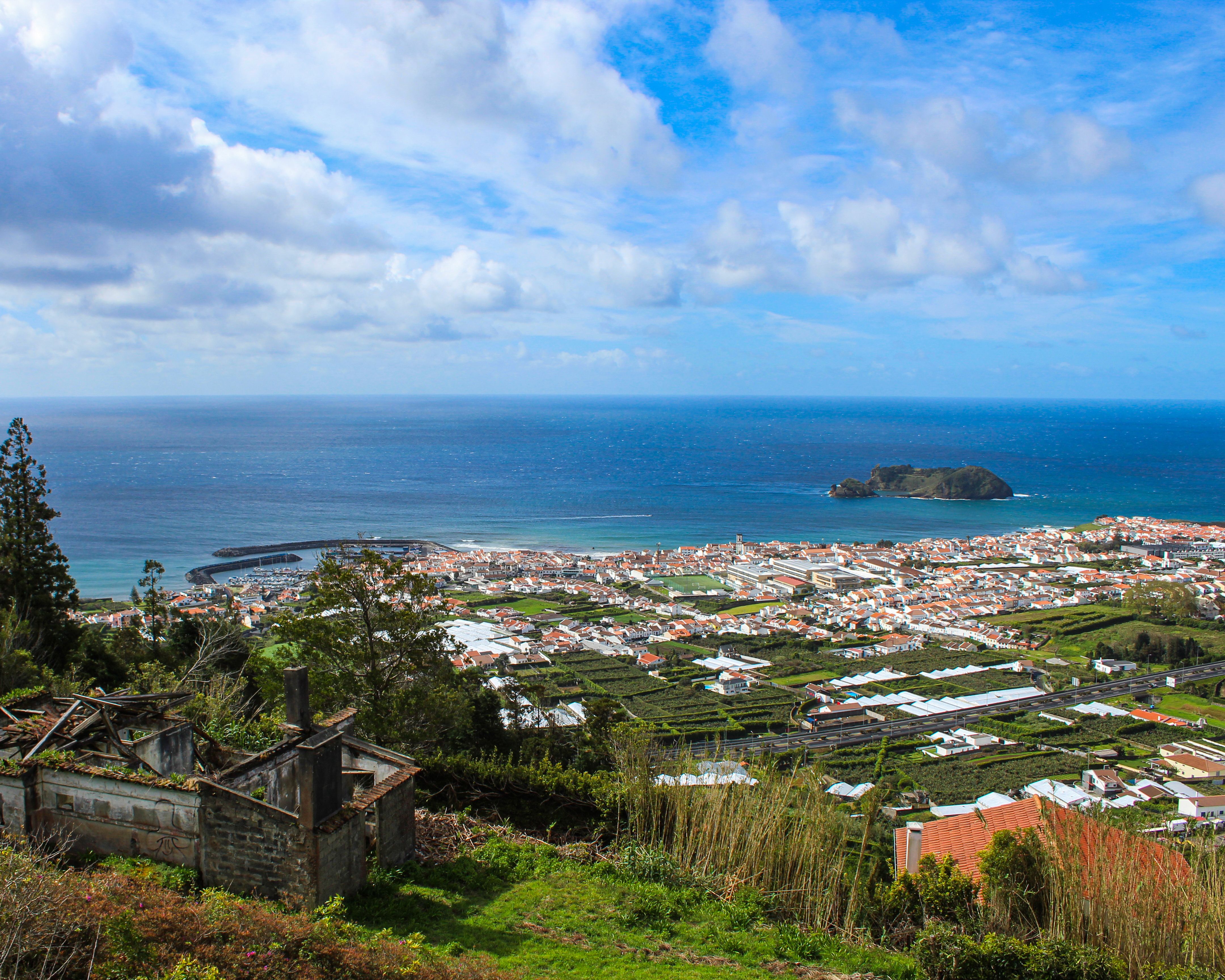 Scenic aerial view of a coastal town in Terceira Island, Azores, with ocean and clouds.