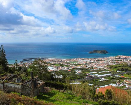 Scenic aerial view of a coastal town in Terceira Island, Azores, with ocean and clouds.