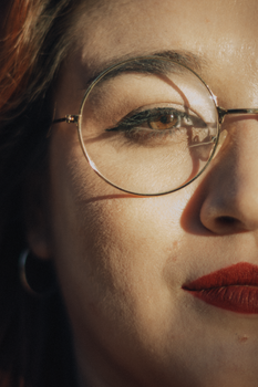Detailed close-up of a woman with glasses and red lipstick in warm sunlight.