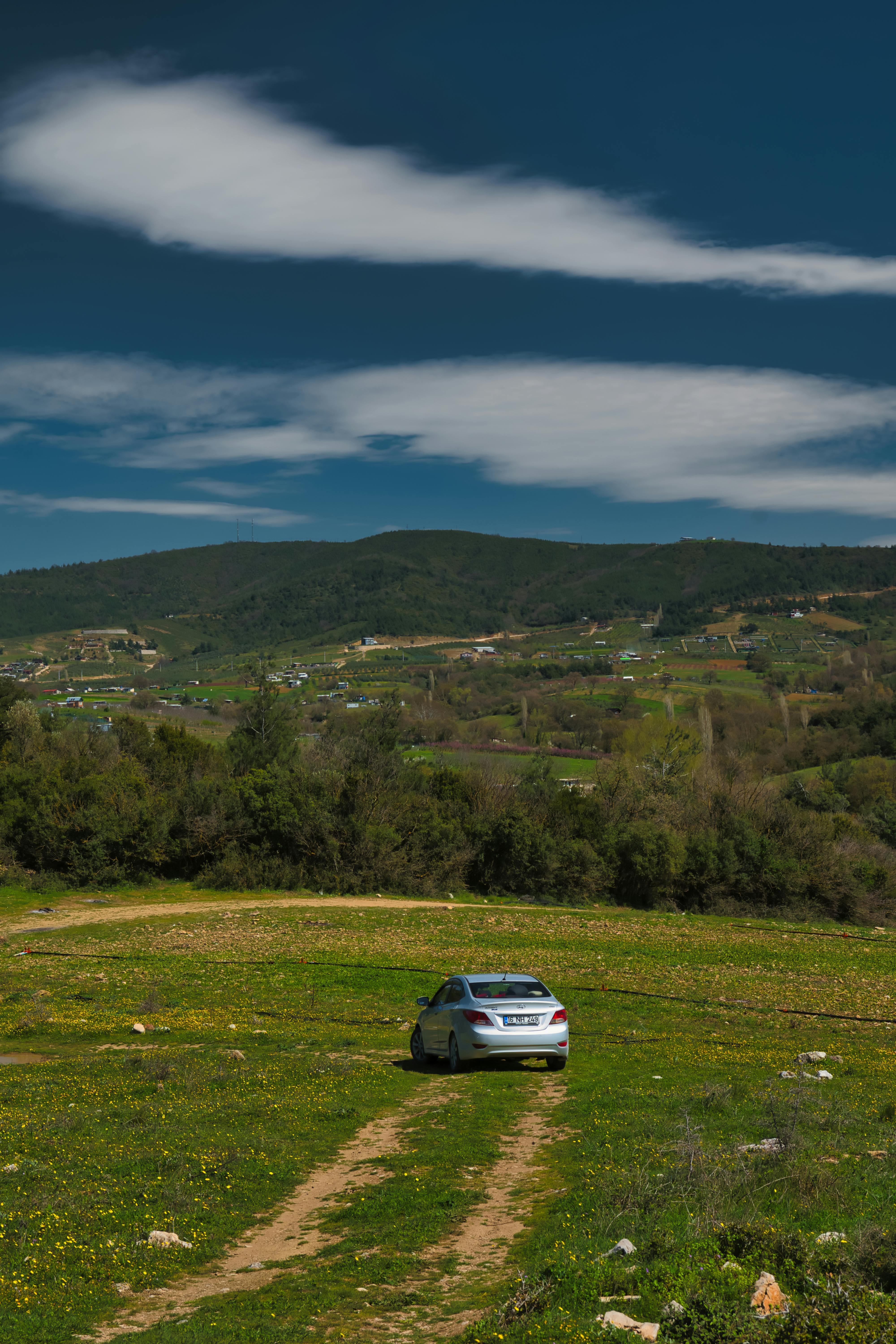 A car on a dirt path in a scenic mountainous landscape under a clear blue sky.