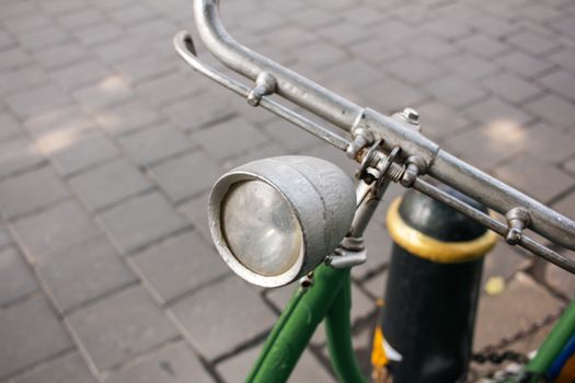 A detailed view of a classic bicycle headlight and handlebars on a paved street.