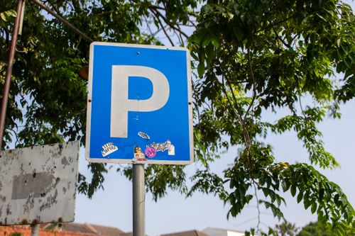 Free A blue parking sign with stickers, set against a leafy urban backdrop, suggesting street parking. Stock Photo