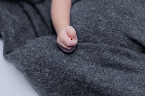 Free A tender close-up of a newborn's hand resting on a soft gray blanket, symbolizing innocence and warmth. Stock Photo