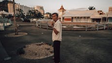 黄昏时分，城市公园里，一位衣着考究的男子以城市建筑为背景，陷入沉思