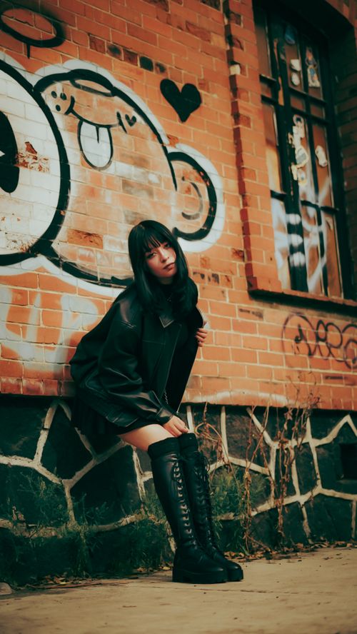 Free Young woman in black attire posing by urban graffiti wall, blending edgy fashion with street art. Stock Photo